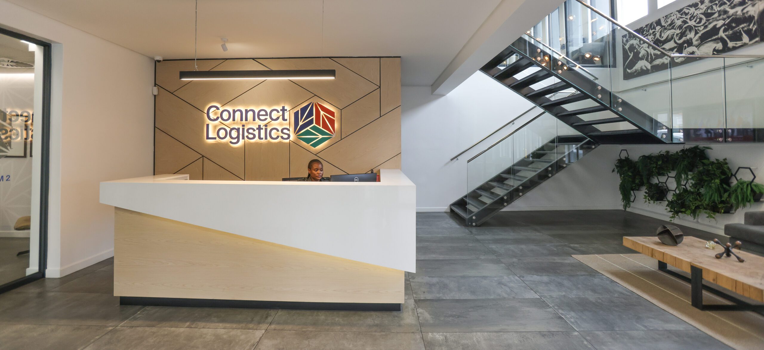 Reception area of Connect Logistics with an attendant, backlit logo on the wall, and a modern staircase.