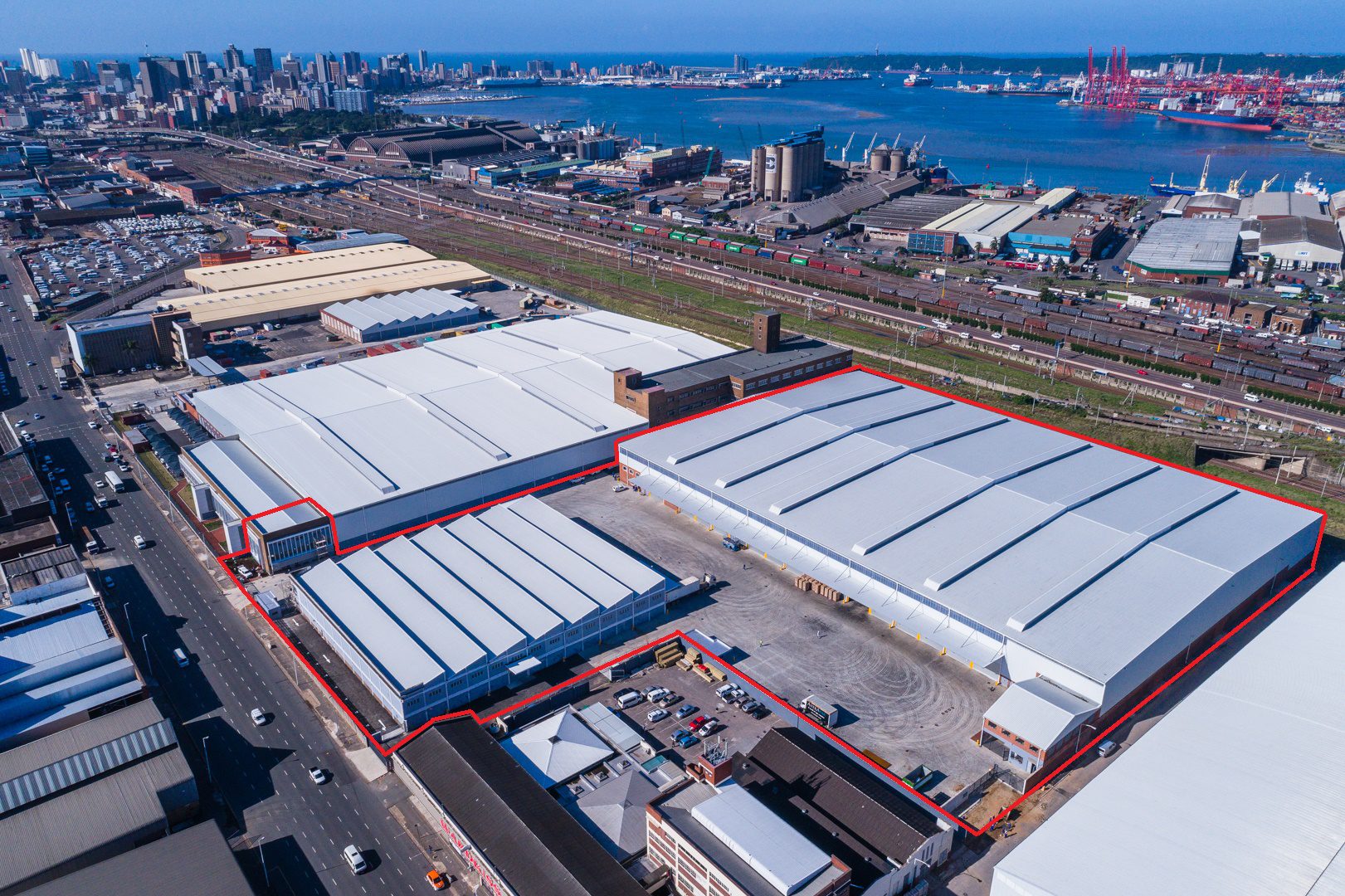 Aerial view of Connect Logistics warehouse complex with red trim by the port and city skyline, indicating a logistics hub.
